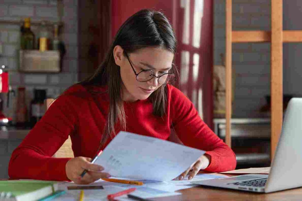 How Assignment Help Brisbane Services Improve Student Performance 1 horizontal shot project manager spectacles red juumper looks attentively documents thinks how attract clients increase income poses against kitchen interior with portable laptop 11zon